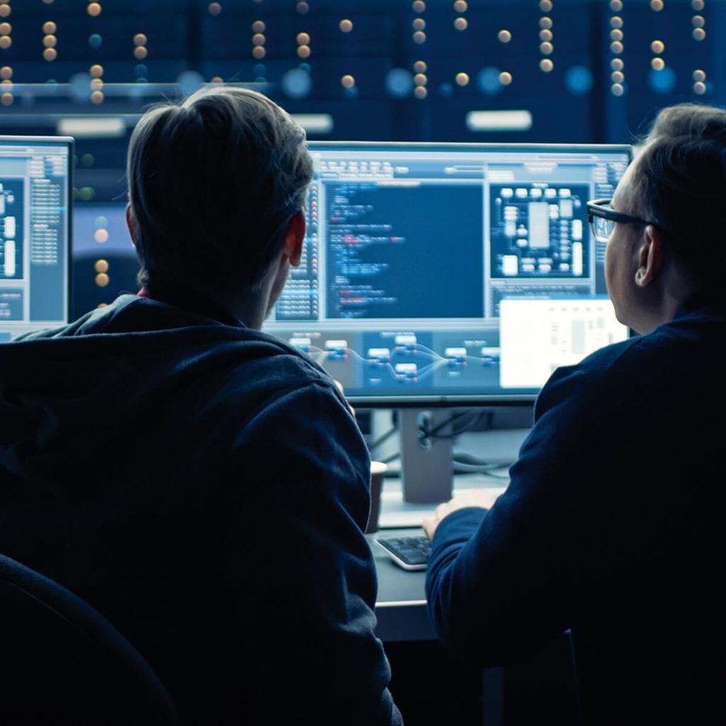 Zwei Männer betreiben nachts am Computerbildschirm Energiemanagement mit dem Ziel, Kosten zu sparen.